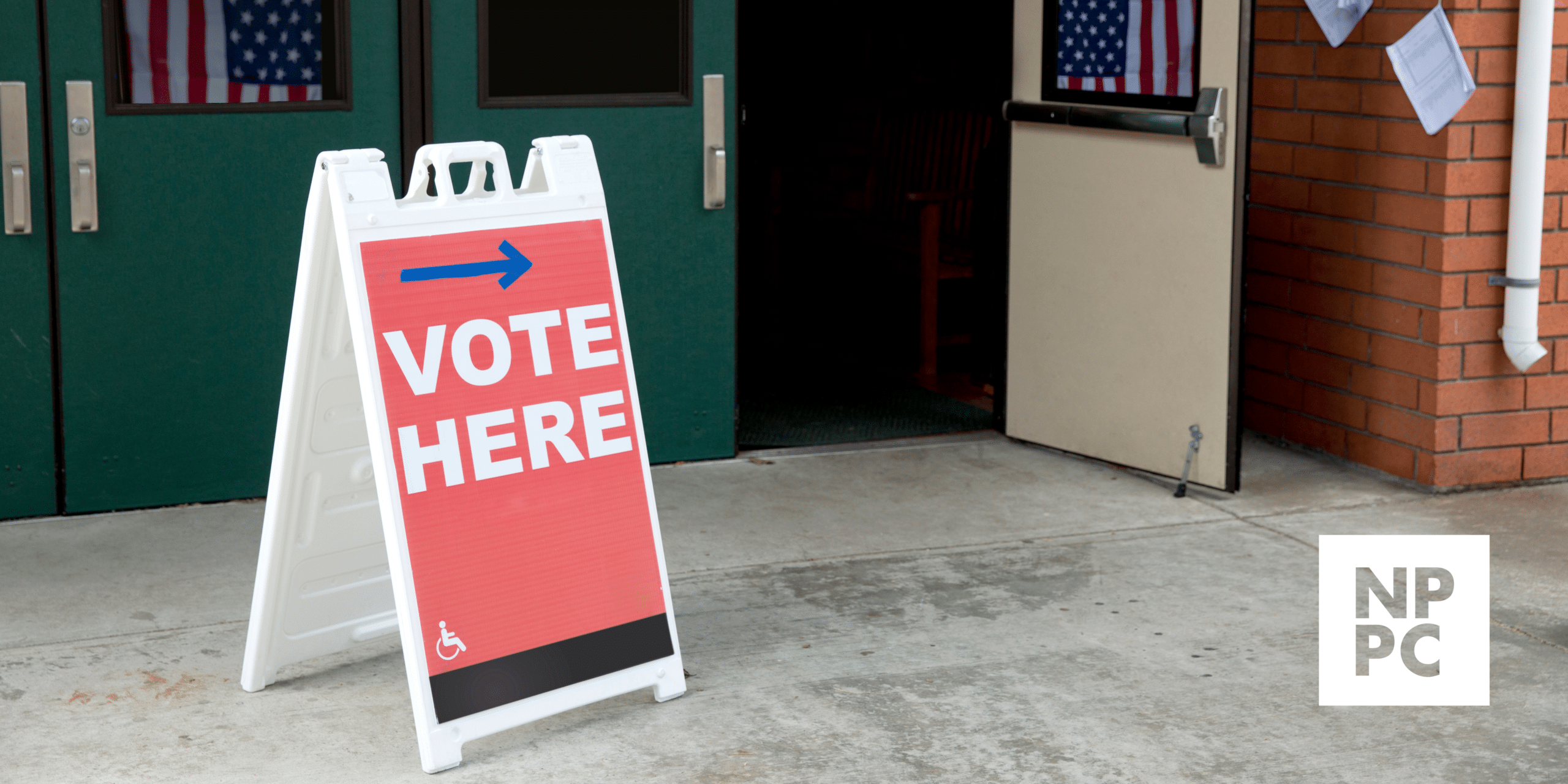 Sign reading "Vote Here" stands outside a set of double doors.